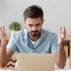 Irritated man looking at laptop screen sitting at the desk