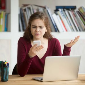 Frustrated female entrepreneur looking at cellphone and shruggin