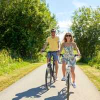 people, leisure and lifestyle concept - happy young couple riding bicycles along road in summer