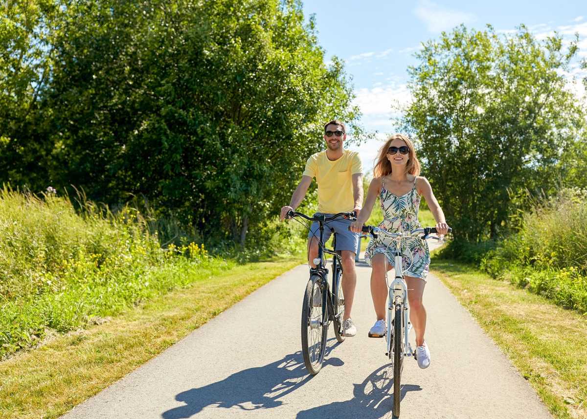 people, leisure and lifestyle concept - happy young couple riding bicycles along road in summer