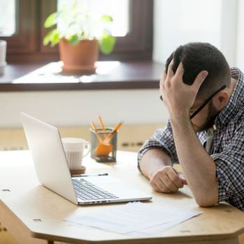 Depressed man looking in his laptop computer receiving bad news.