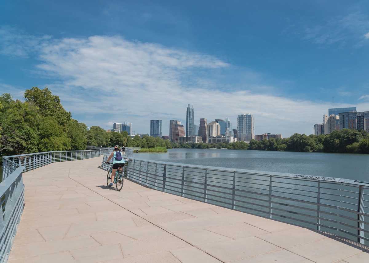 People biking running walking along Colorado River waterfront boardwalk near downtown Austin, Texas in summer day